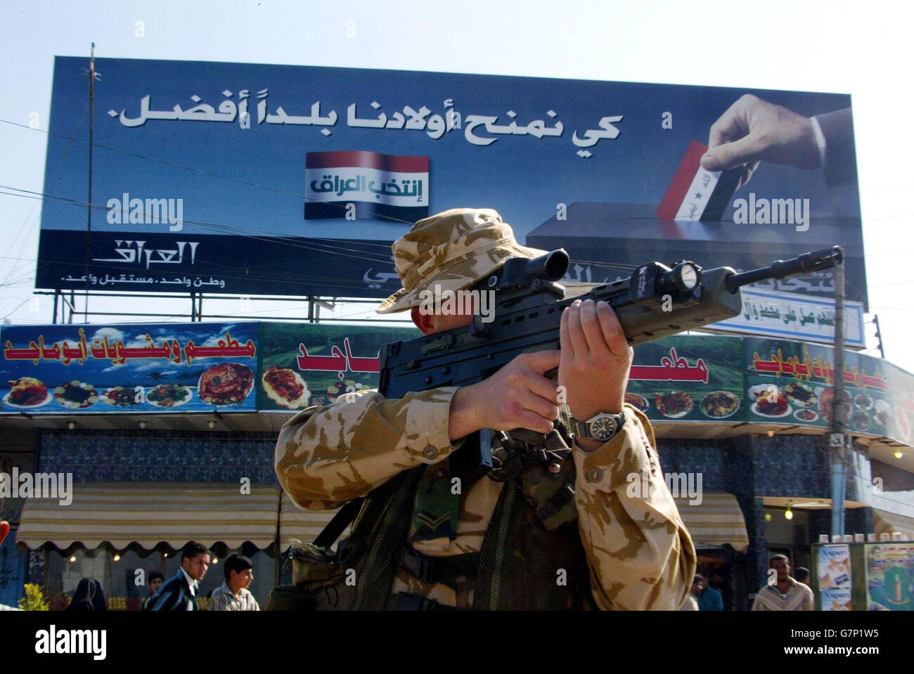 A soldier from the Royal Artillery aims his SA80 in front of an election billboard whilst on patrol in Az Zubayr. Stock Photo
