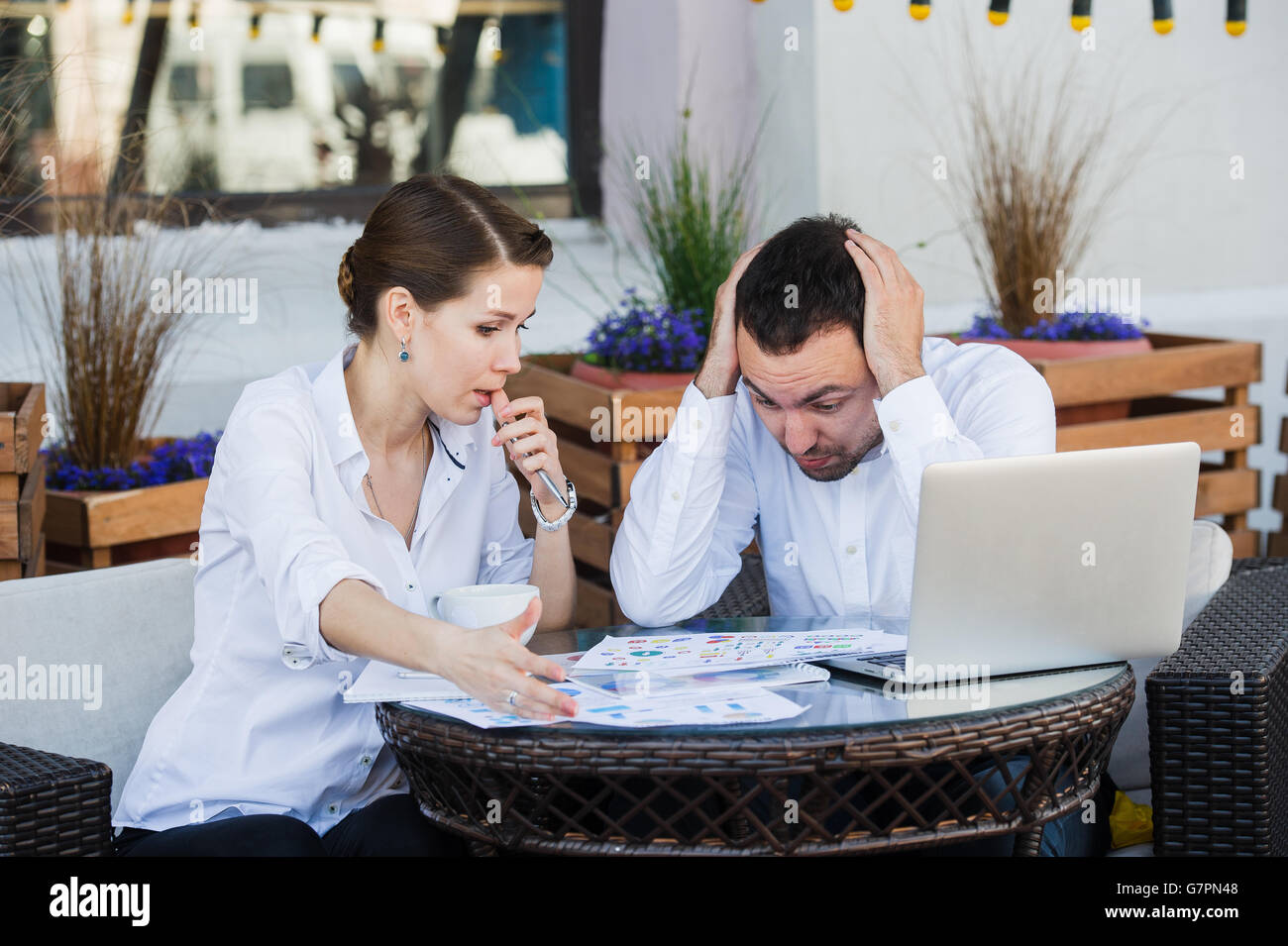 Male and female business colleagues working together on a hard problem at outdoors cafe. They have strained expression on their faces Stock Photo