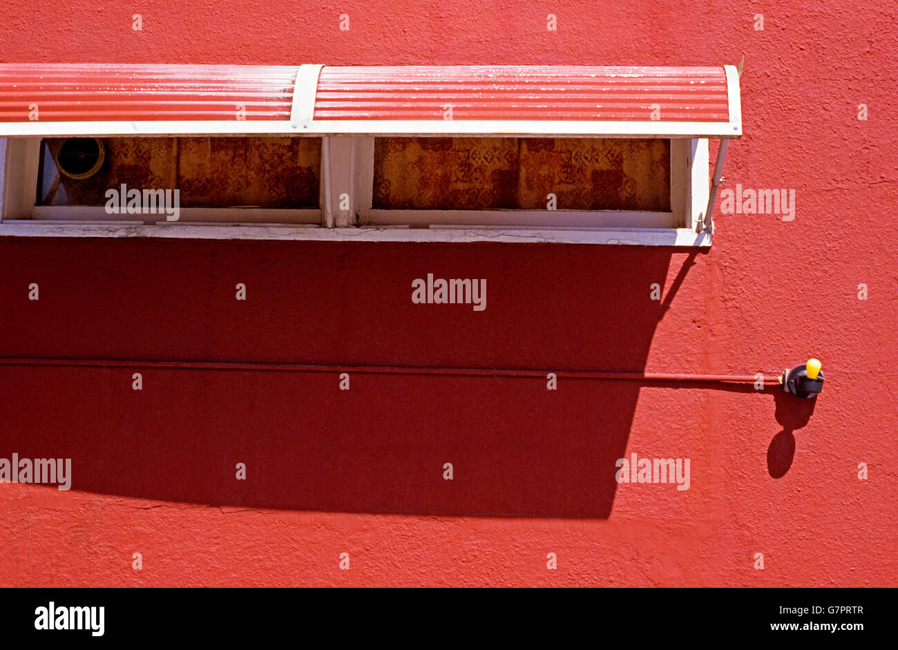 Side of building with yellow light bulb  and window shades against red building, street scene, urban scene Stock Photo