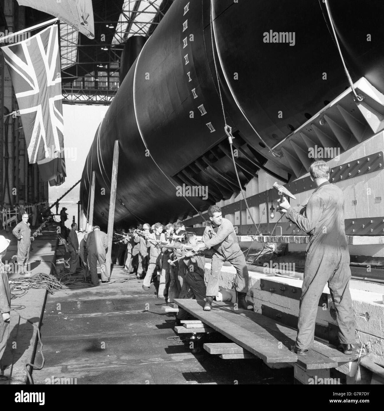 The setting up ceremony at HM Dockyard, Chatham, Kent, as shipwrights, working in unison, raise the submarine Okanagan on the launching way by hammering wedges under the launching cradle. She will be named by Madame Cadieux, wife of the Associate Minister of National Defence for Canada. Okanagan is the third and last of the present series of Oberon class submarines built for Canada. She will be ready for service in about a year. Stock Photo