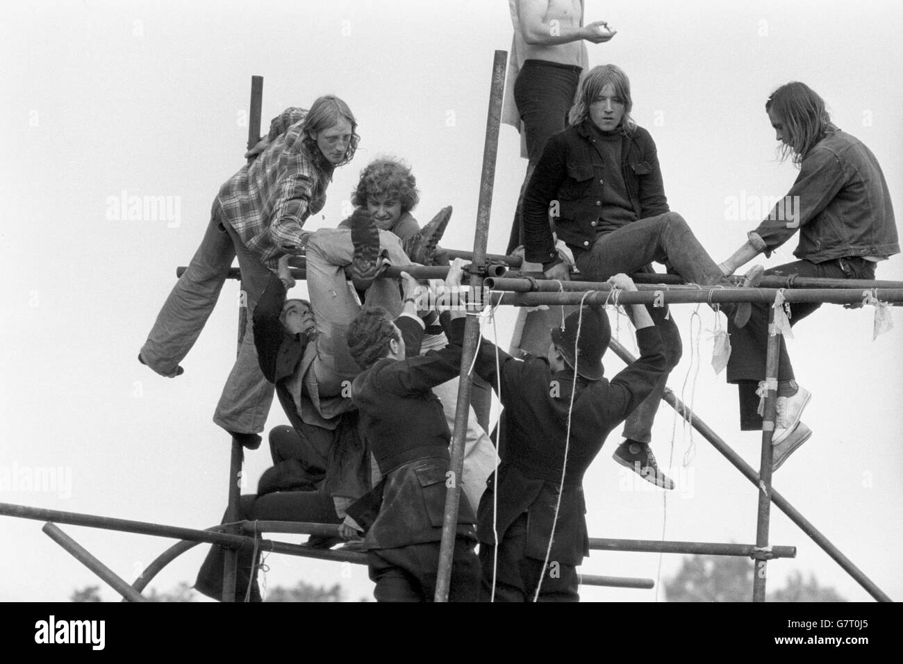 Free Pop Festival fans clamber up scaffolding poles in their bid to evade the arm of the law at Windsor Great Park after 600 police moved in to break up the event which got underway last weekend. Policemen's uniforms and fans clothes were torn in some scuffles. Stock Photo