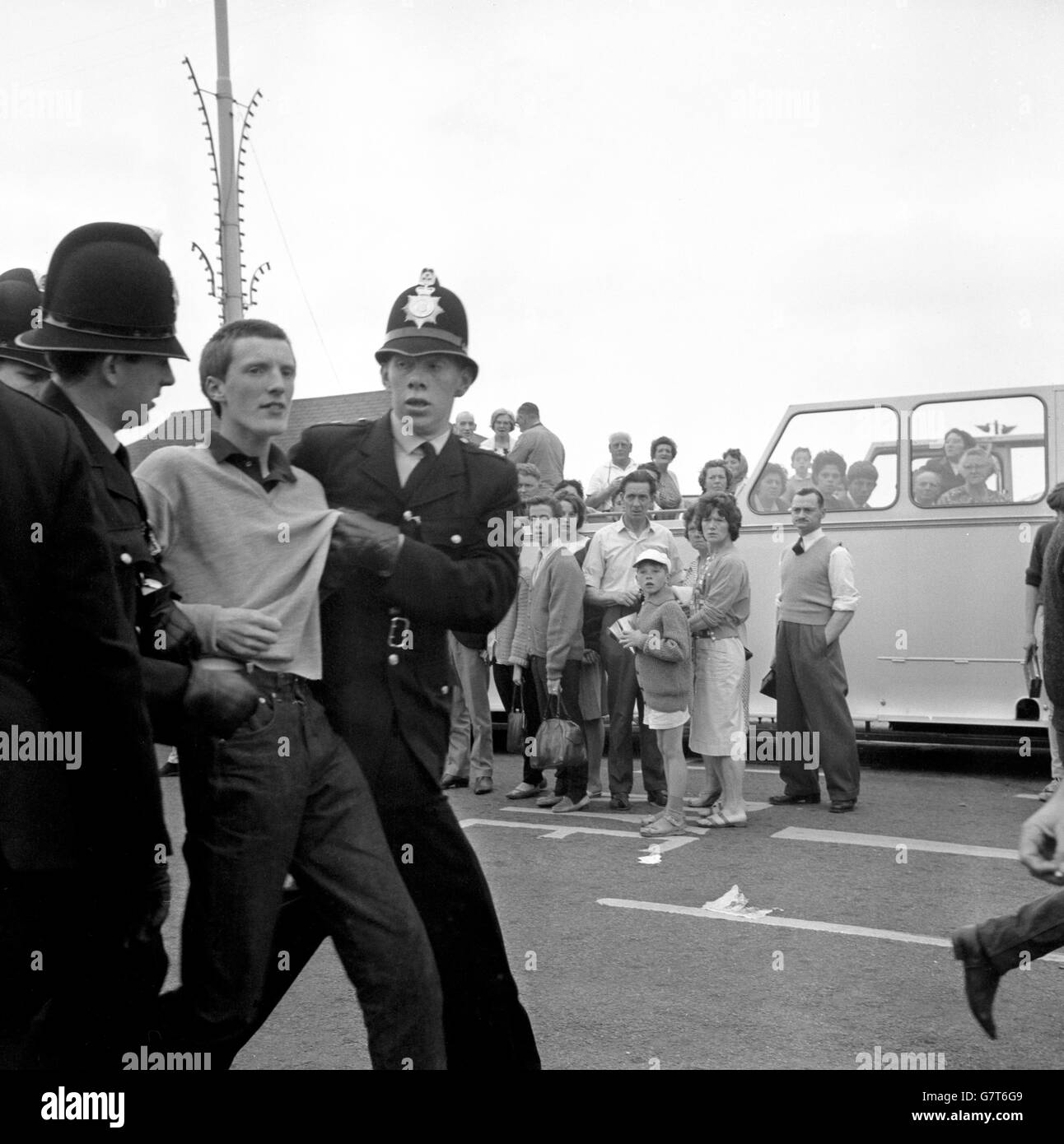 Uniformed police officers holding a young man in Hastings, Sussex, after an incident involving a family saloon car. Extra police, 69 flown in from the Metropolitan force, were drafted to Hastings after sporadic outbreaks of trouble. Mods and Rockers descended on the town, mostly by scooters and motorcycles, but some also by train. Stock Photo