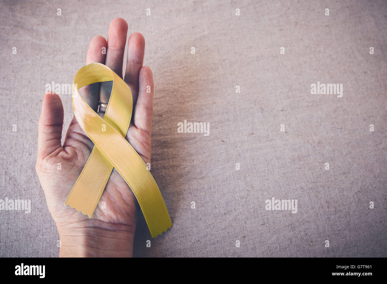 Yellow Ribbon on hand, copy space toning background, Bone cancer awareness Stock Photo