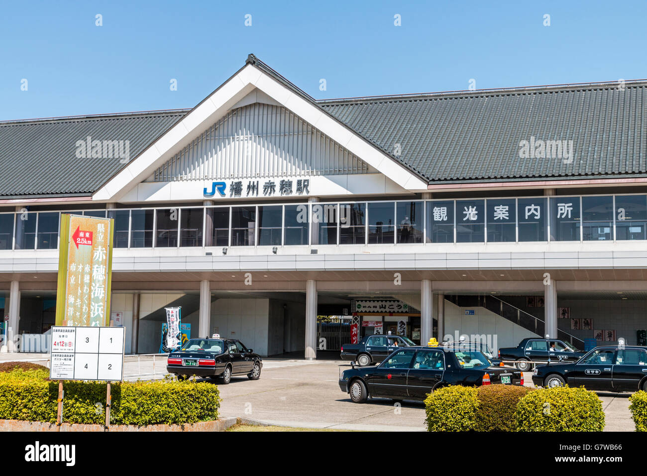 Japan, Ako. JR. Japanese railway station building with JR logo and kanji name. Taxies waiting in front. Daytime, sunshine, blue sky. Stock Photo