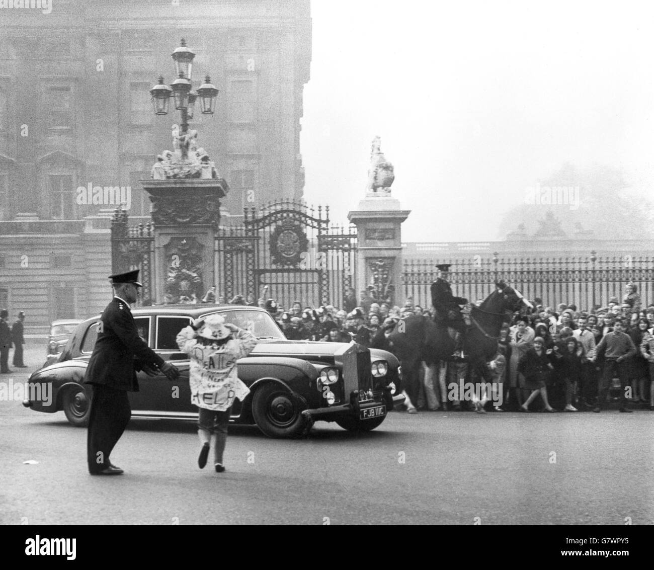 A police officer tries to stop a girl fan making a break for the Beatles' Rolls-Royce as the group leave Buckingham Palace after attending the Investiture. In the background, a mounted policeman holds back a section of the huge crowd which gave the Beatles a screaming send-off probably unprecedented outside the Palace. The Beatles had received from the Queen their insignia as Members of the Order of the British Empire. Stock Photo