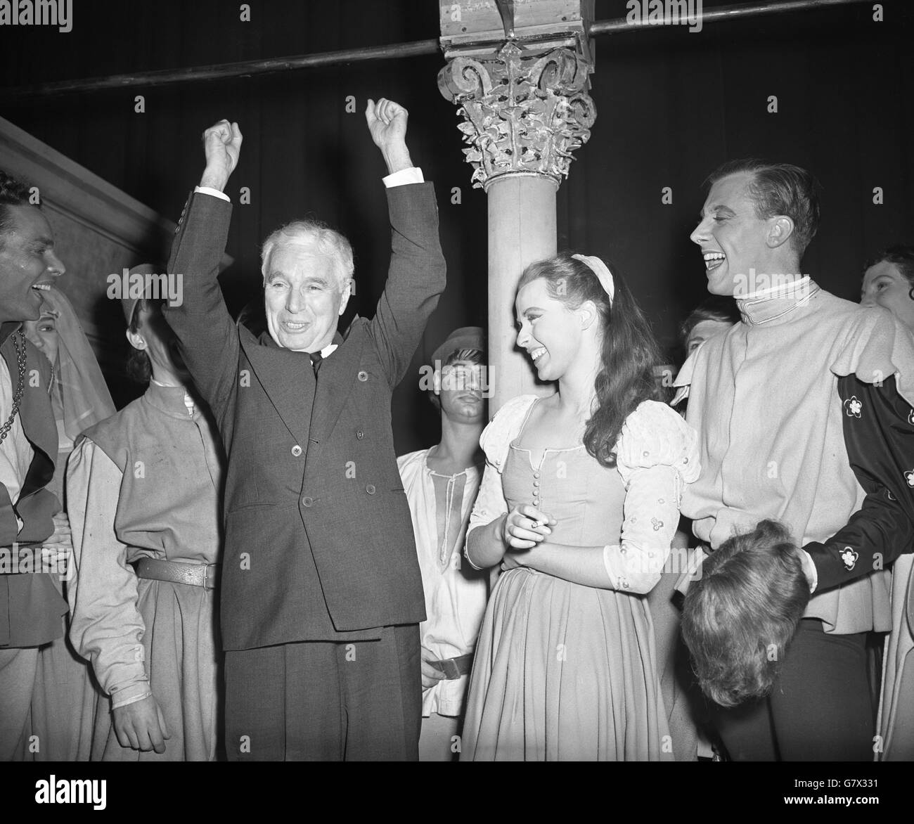 Charlie Chaplin raises his arms in salute to the cheering Old Vic crowd as he stands alongside actress Claire Bloom on the stage of the theatre in Waterloo Road, London, where he saw his 'Limelight' leading lady in a performance of Shakespeare's 'Romeo and Juliet'. Stock Photo
