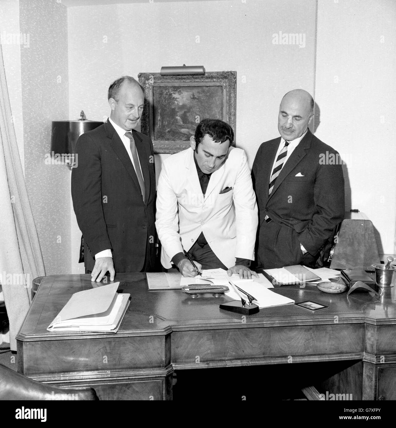 Lionel Bart signs the contract for the film version of his long-running musical 'Oliver' in London. Watching are John Woolf (l), chairman of Romulus Films, which will make the picture, and Maxwell Setton, managing director of Columbia (British) Productions. Stock Photo