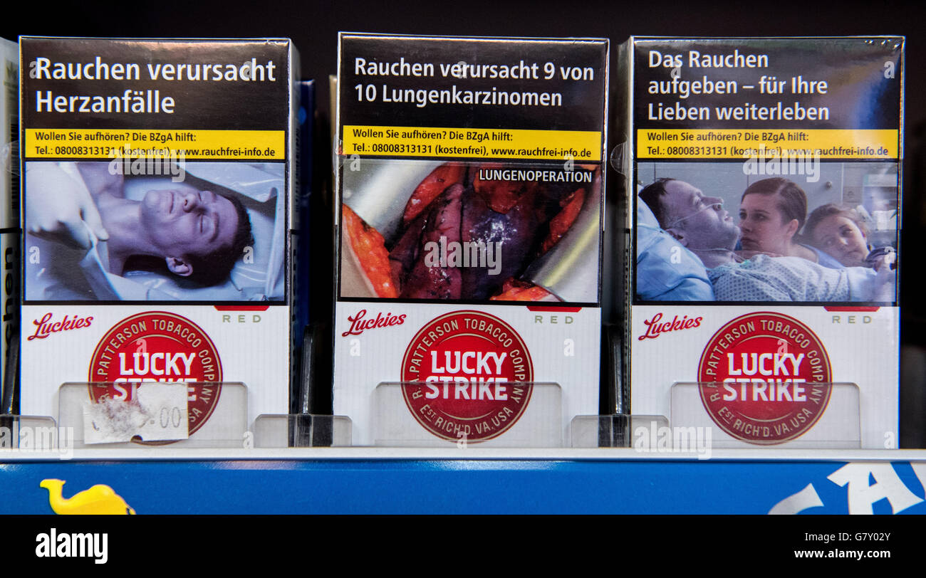 Hamburg, Germany. 26th June, 2016. ILLUSTRATION - Packs of 'Lucky Strike' cigarettes with shock photos and the warning labels 'smoking causes heart attacks, ' (L-R) 'smoking causes 9 out of 10 cases of lung cancer' and 'quit smoking - keep living for your loved ones' can be seen on a shelf in a kiosk in Hamburg, Germany, 26 June 2016. According to a representative survey, the majority of Germany don't believe in the deterring effect of shock photos on packs of cigarettes. Photo: Daniel Bockwoldt/dpa/Alamy Live News Stock Photo