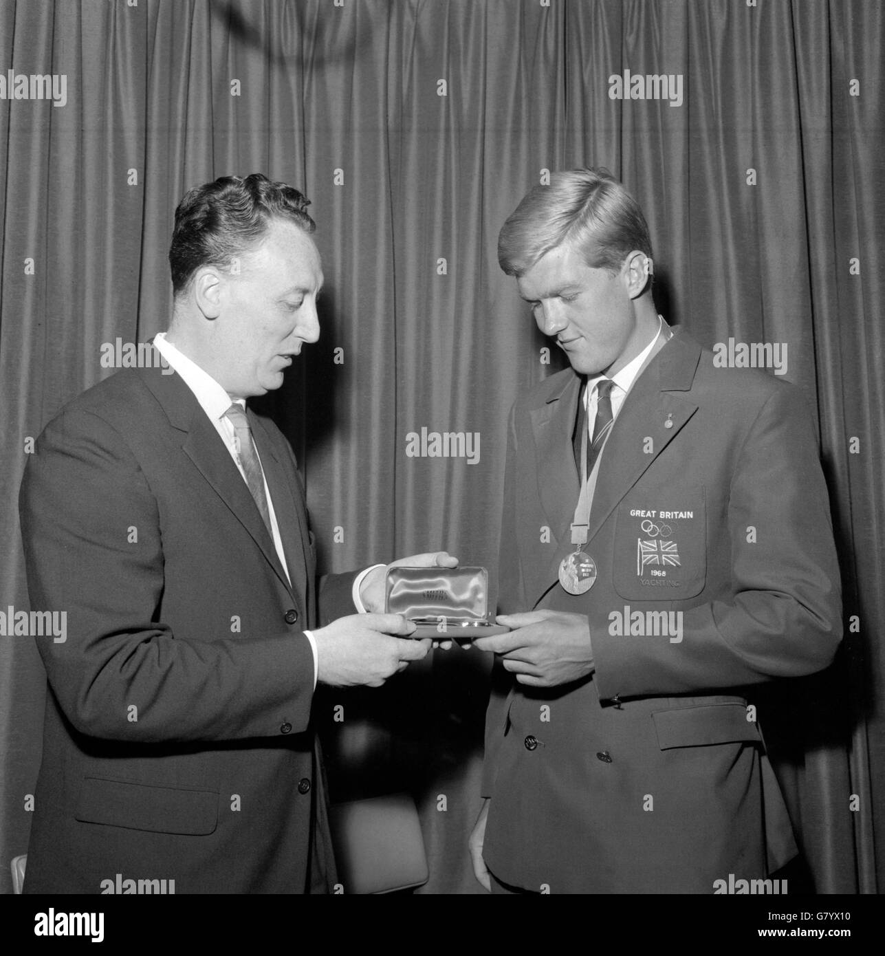 Gold medallist yachtsman, Iain MacDonald-Smith (r), was presented with a gold watch by Clive Middleton, the marketing director for Smiths Industries Clocks and Watch Division Ltd, at Heathrow Airport after arriving from Mexico. Stock Photo