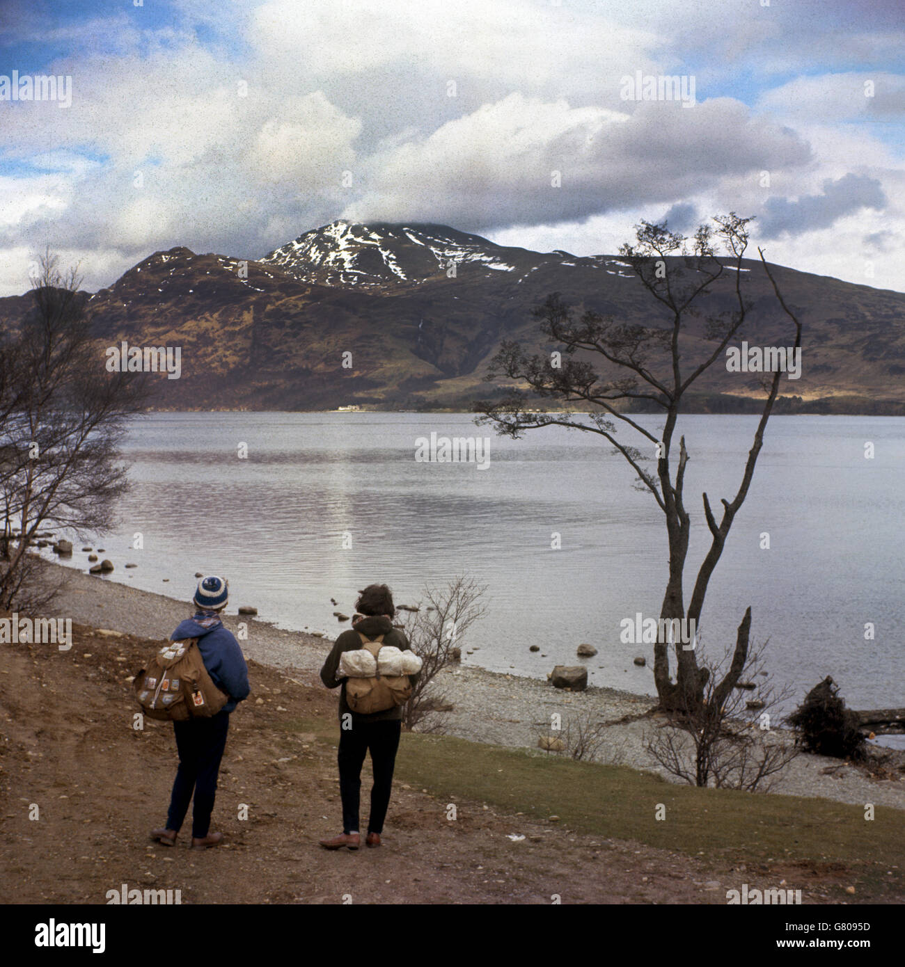 Two walkers looking at the mountain of Ben Lomond over Loch Lomond, Tarbet, Scotland. Stock Photo