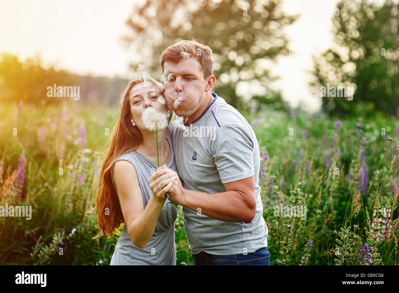 Young happy couple blowing together dandelions, outdoor in nature Stock Photo