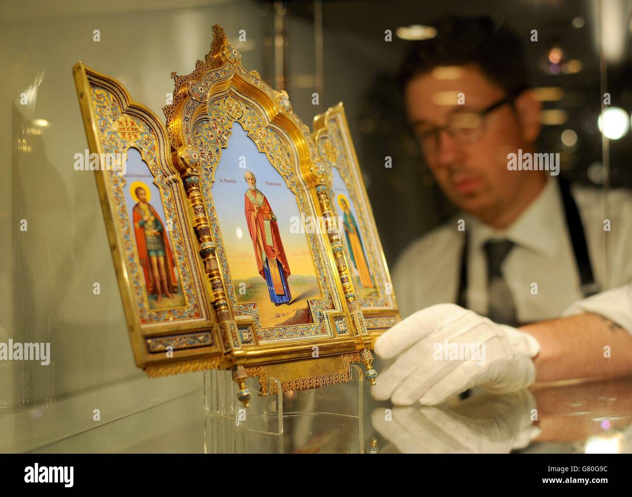 A gallery staff member adjusts an imperial silver-gilt and cloisonne enamel triptych icon (1886) by Khlebnikov, Moscow, estimated at £100,000 to £150,000 during a photocall for Sotheby's sale of Russian Works of Art, Faberge and Icons in New Bond Street, London. Stock Photo