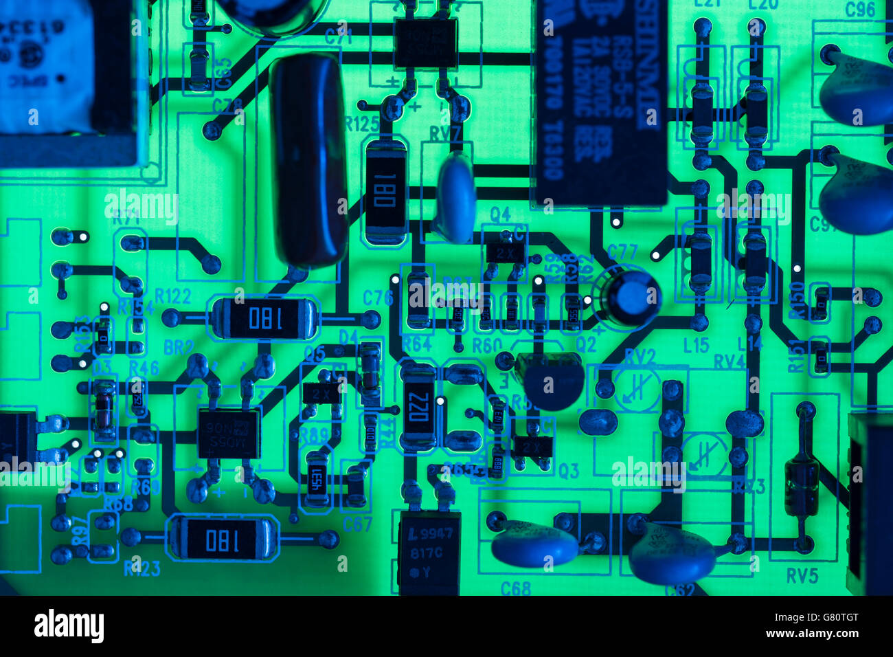 Technology concept . Circuit board / pcb showing components lit with blue and green light. Wiring inside computer, circuit close up, electronics. Stock Photo