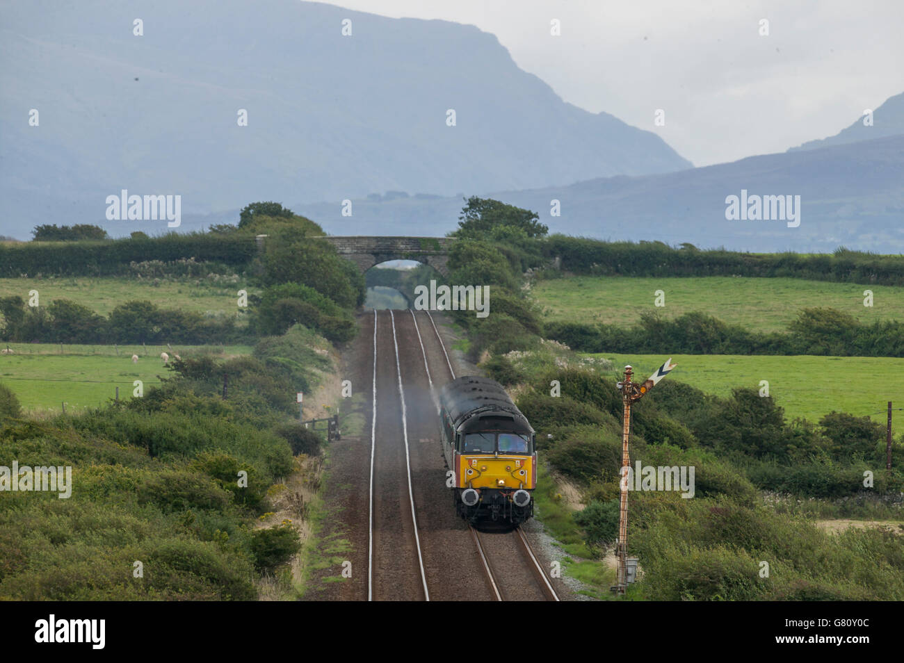 Class 47 heads across Anglesey bound for Holyhead. The mountains of Snowdonia are visible in background. Stock Photo
