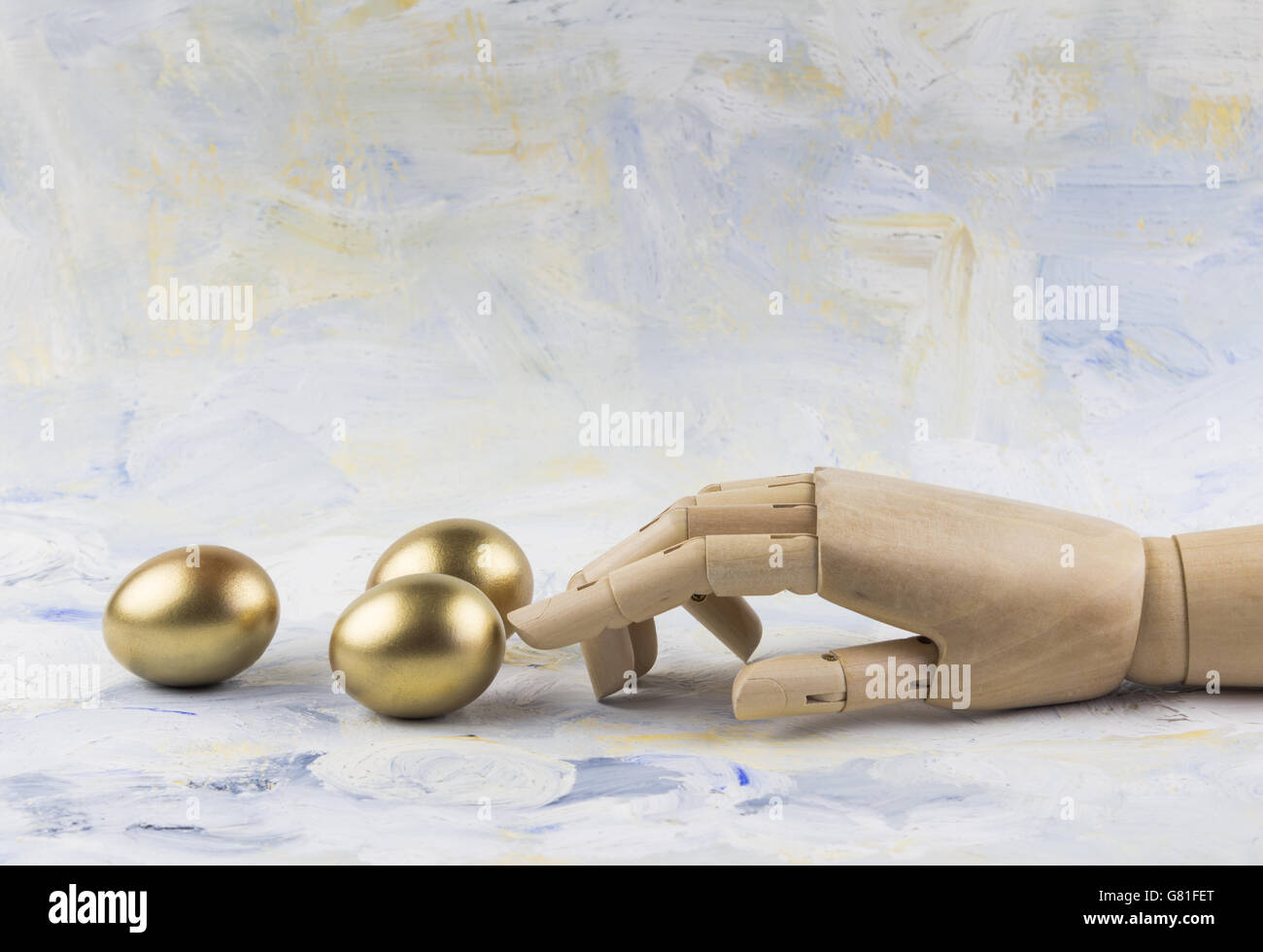 Three golden eggs touched by wooden puppet finger against painted sky background Stock Photo