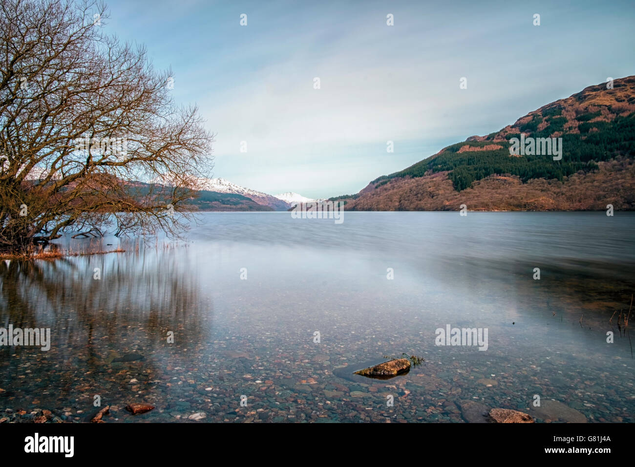 Long exposure of calm waters of Loch Lomond with snow covered mountains in the distance Stock Photo