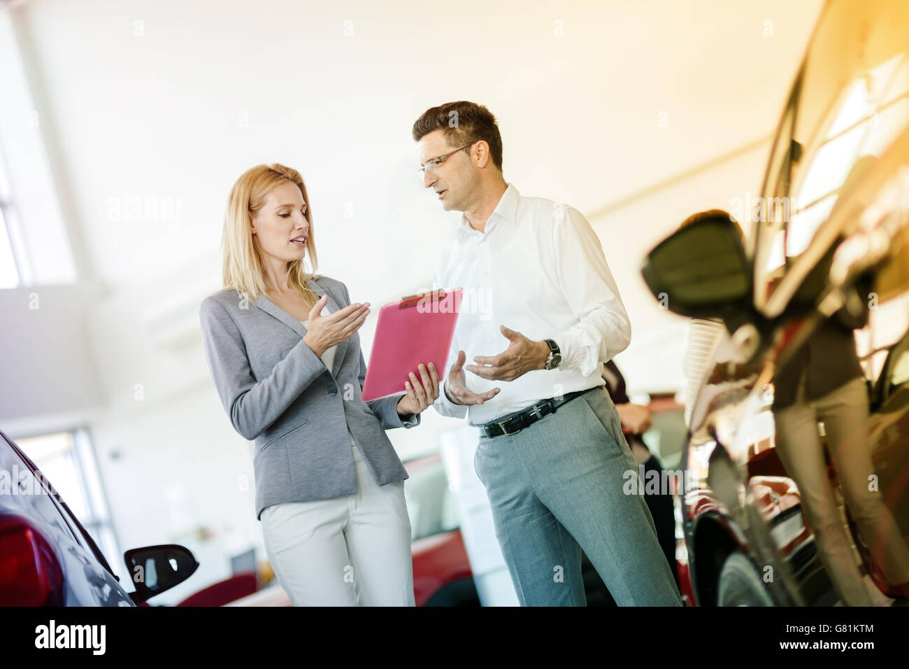 Salesperson showing vehicle to potential customer in dealership Stock
