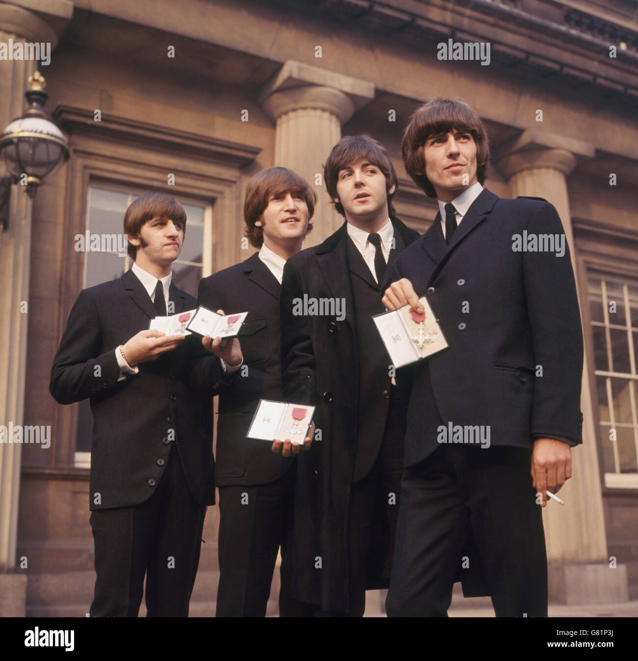 The Beatles showing their MBE Insignias in forecourt after receiving them from the Queen. L-R Ringo Starr, John Lennon, Paul McCartney and George Harrison. Stock Photo