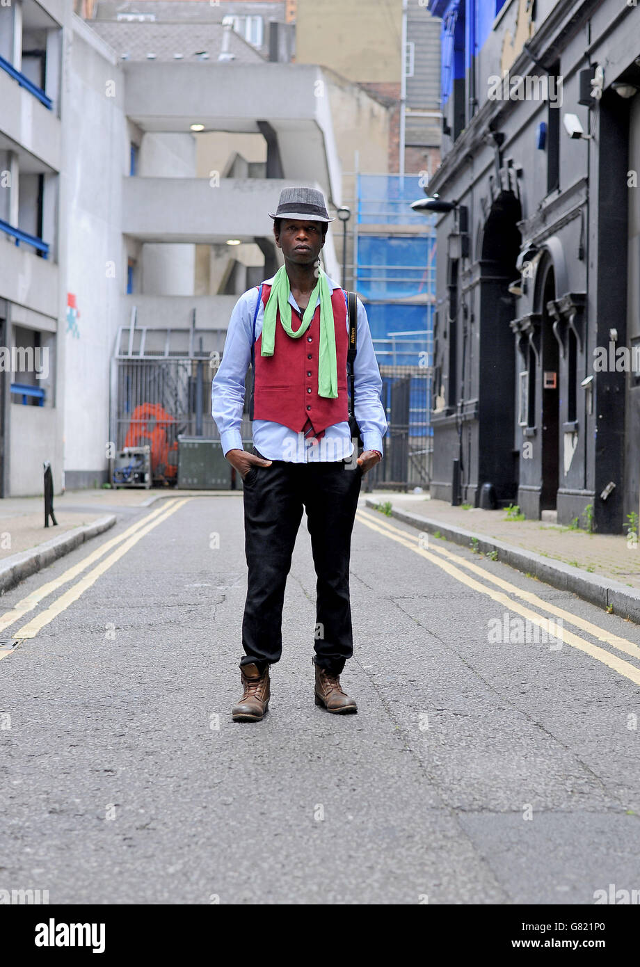Zokaya Kamara of Sidewalk Darlings wears a Calvin Klein fedora hat, Blue Inc scarf and vintage waistcoat, T.M.Lewin shirt, Mark Taylor trousers and Dockers biker boots outside the Old Sorting Office, London as he attends a London Collections: Men event. Stock Photo