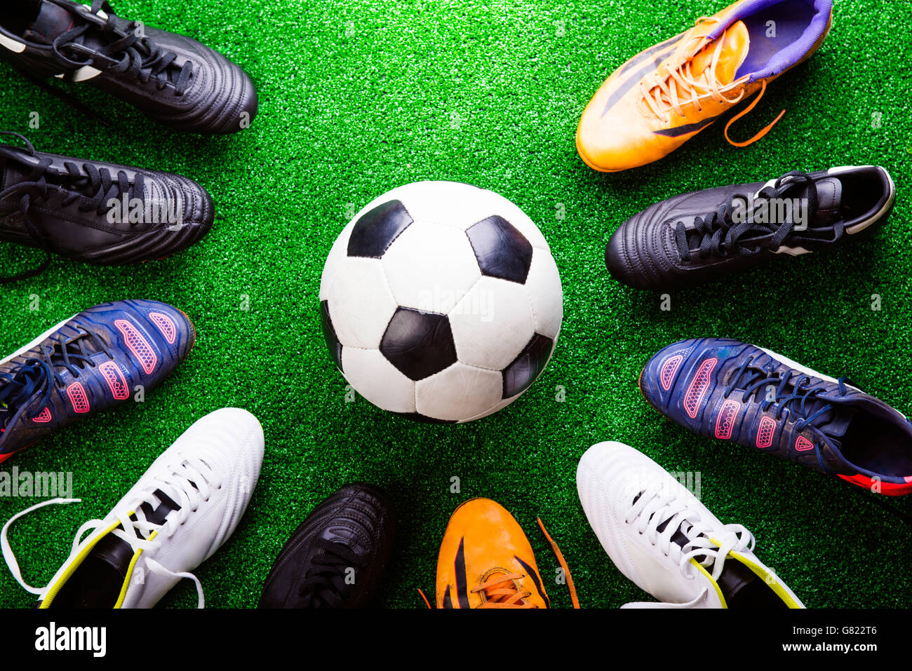 Soccer ball and cleats against green artificial turf, studio sho Stock