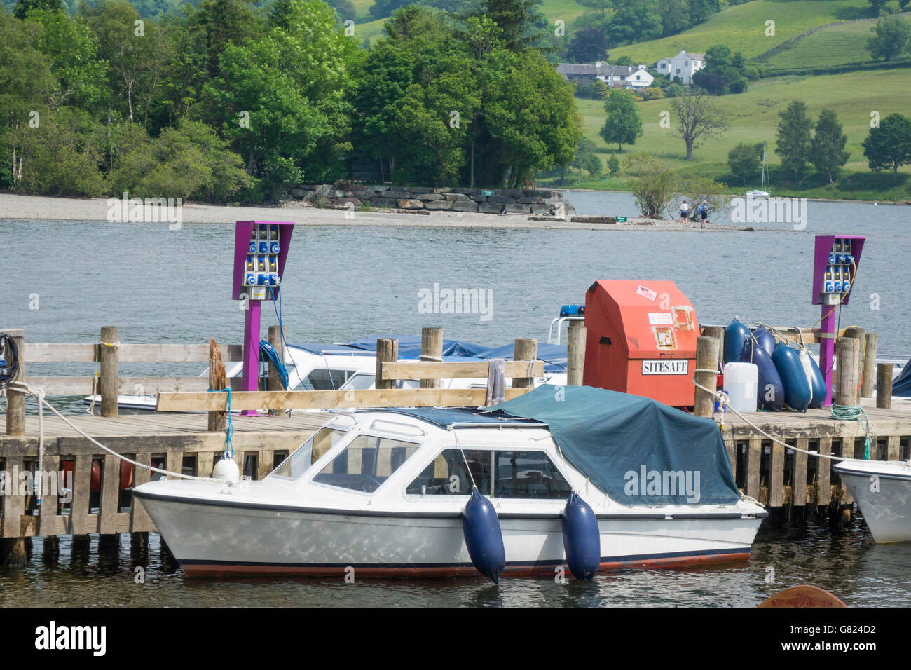 Electric powered small motor boats for hire with charging points on the jetty at Coniston Water Cumbria England Stock Photo