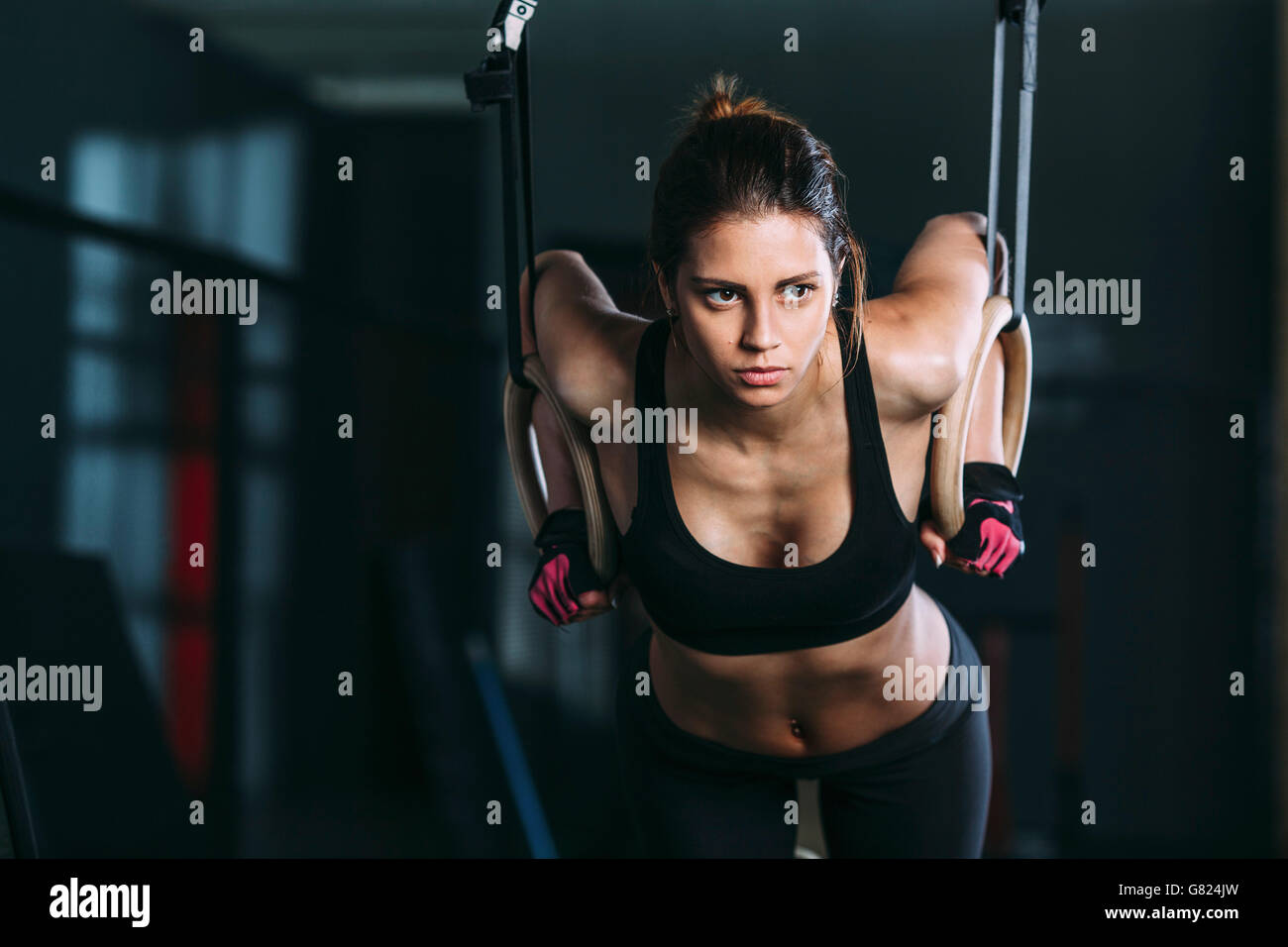 Front view of woman hanging on gymnastic rings at gym Stock Photo