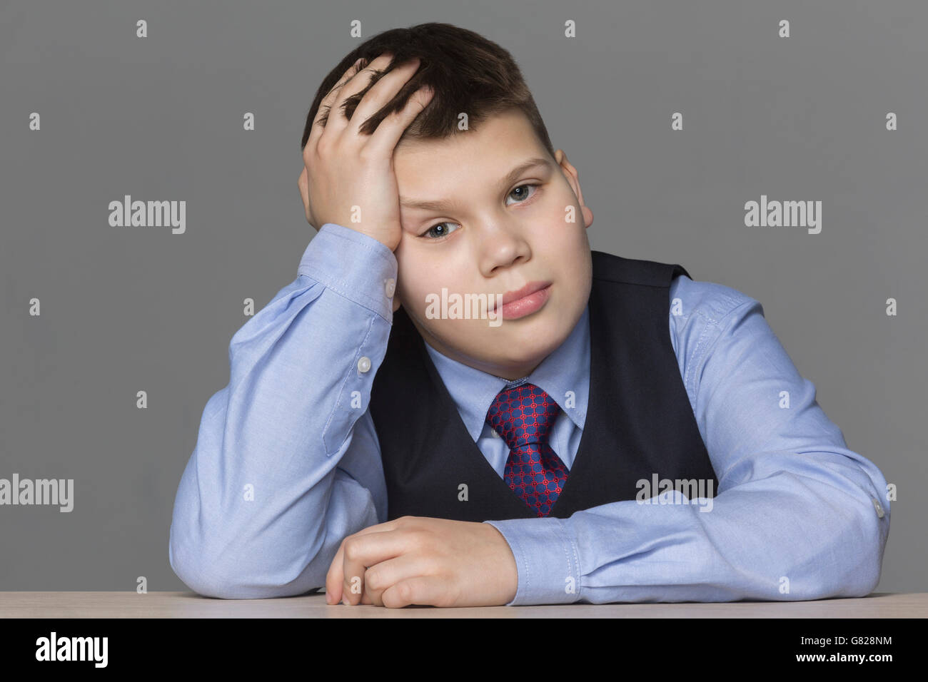 Portrait of boy with head in hand against gray background Stock Photo