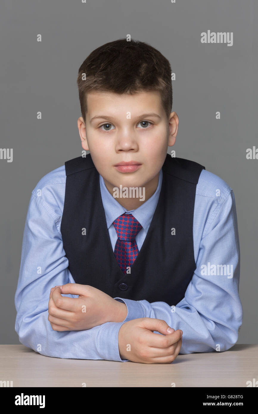 Portrait of confident boy leaning on table against gray background Stock Photo