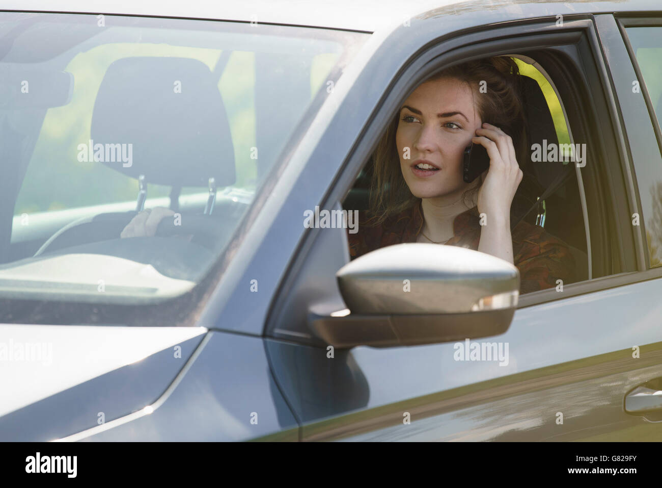 Woman talking on mobile phone while driving car on sunny day Stock Photo