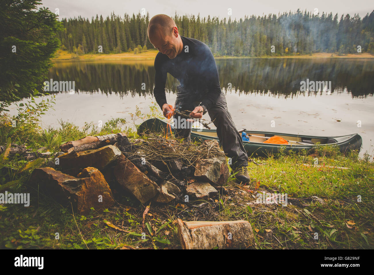 Happy hiker preparing food over bonfire at lakeshore in forest Stock Photo