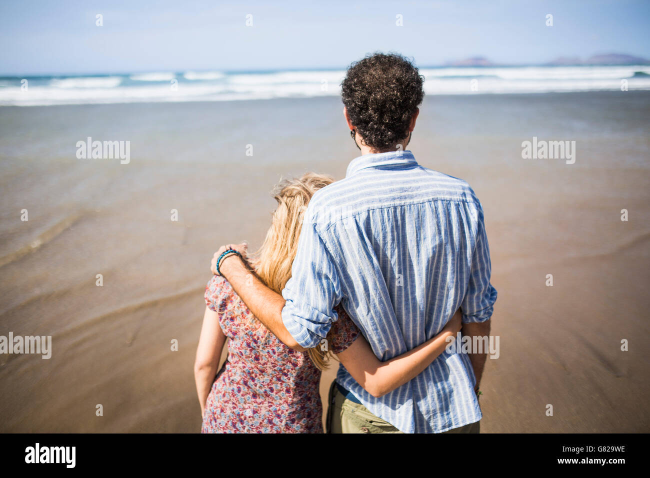Rear view of loving couple standing arm around at beach Stock Photo