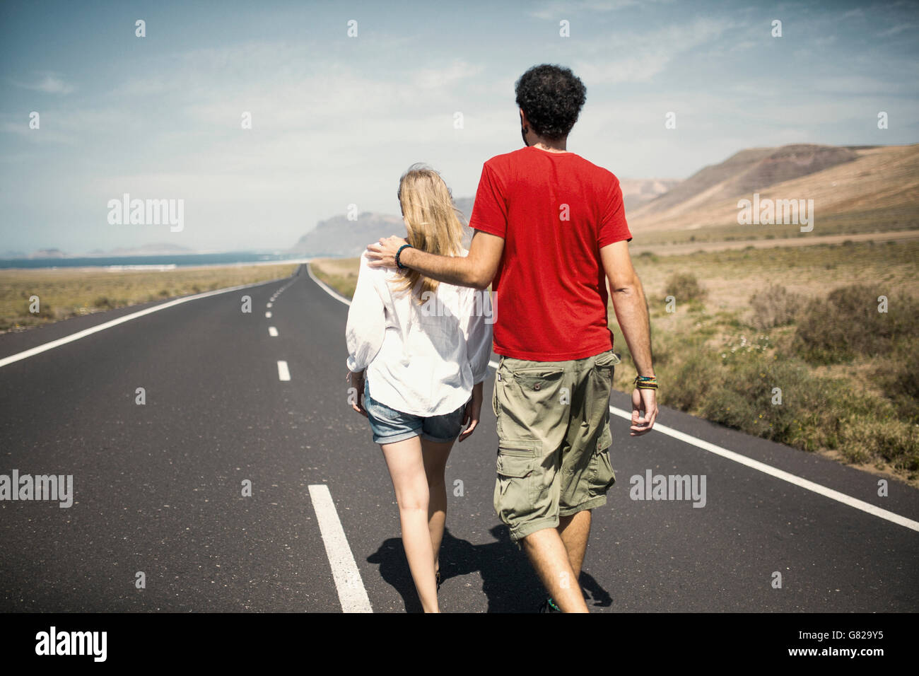 Rear view of couple with arm around walking on road Stock Photo