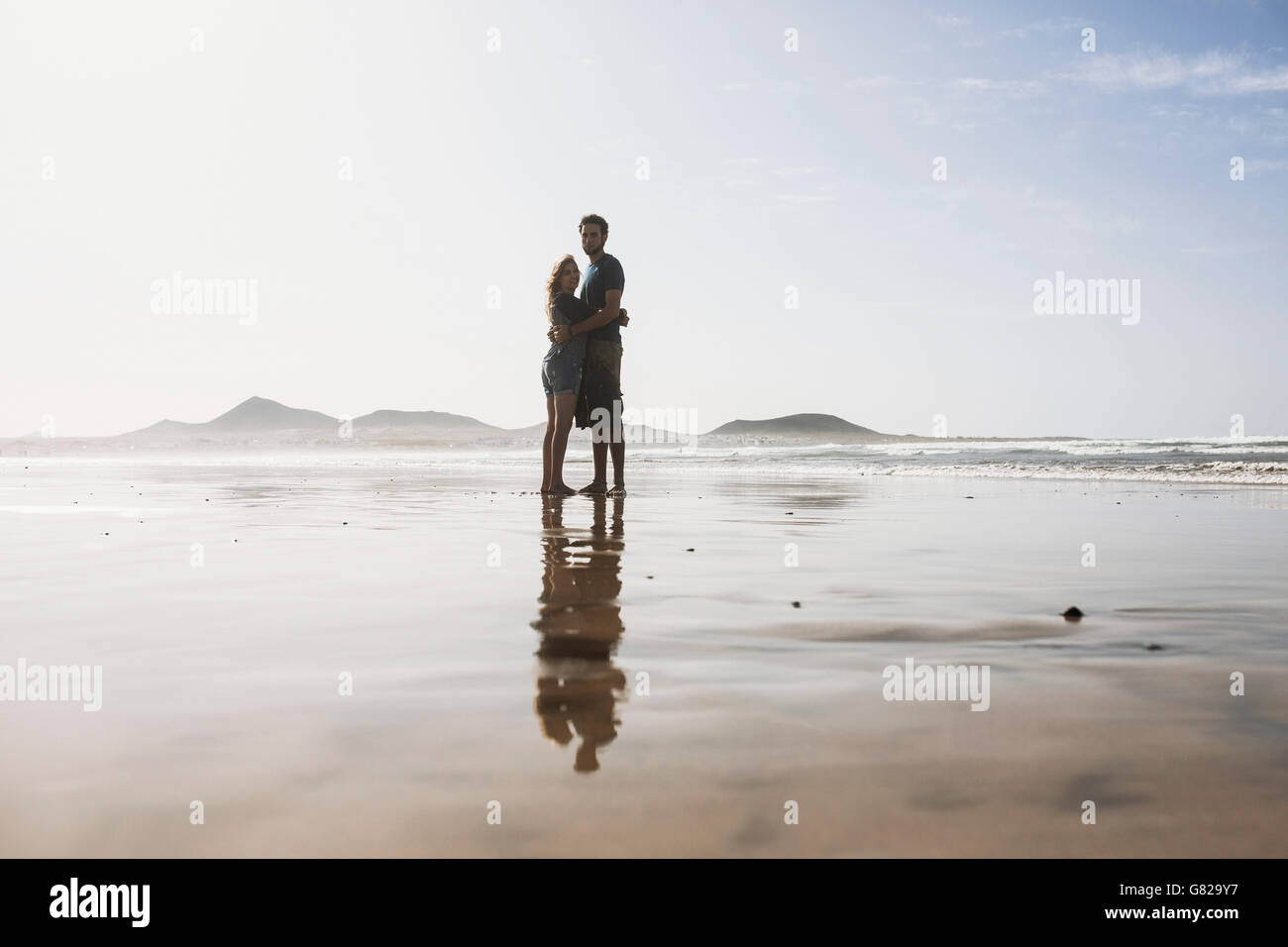 Full length of loving couple embracing at beach on sunny day Stock Photo