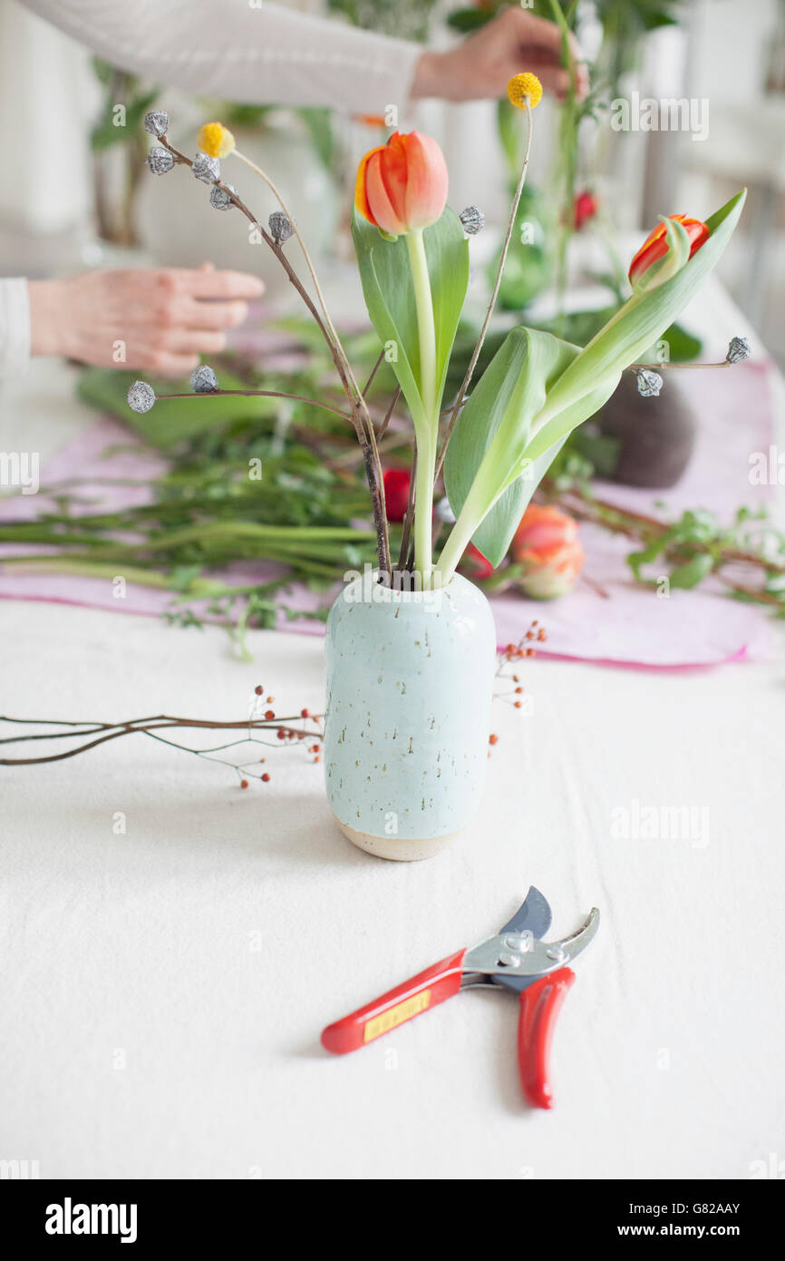 Pruning shears by vase with woman arranging flowers in background at home Stock Photo
