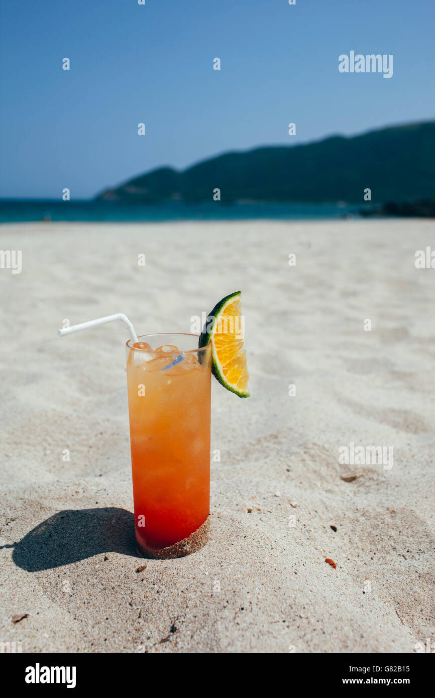 Glass of refreshment on sand at beach during sunny day Stock Photo