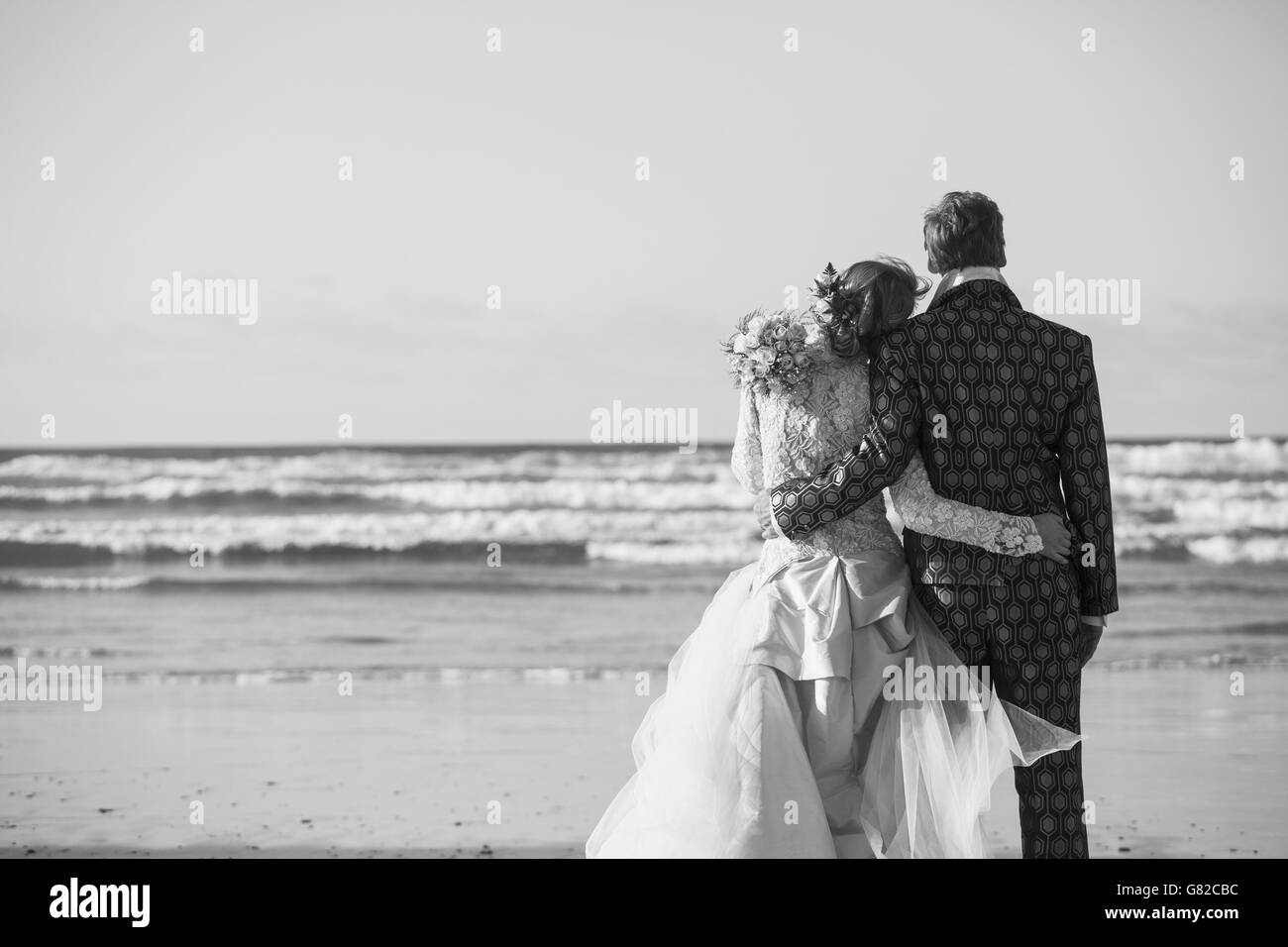 Rear view of bride and groom standing arm around at beach Stock Photo