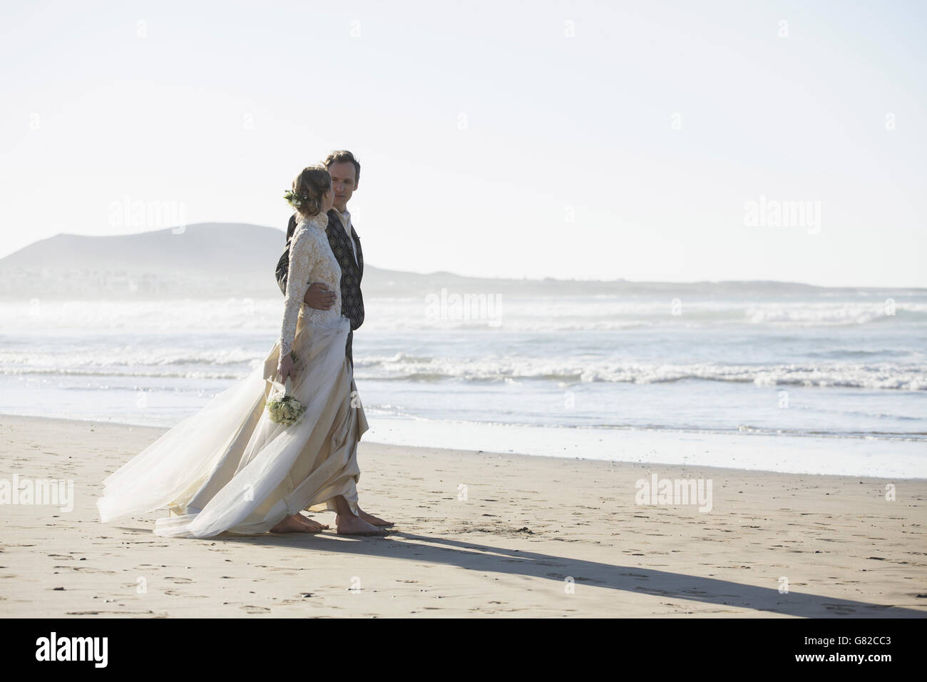 Full length of loving bride and groom walking at beach Stock Photo