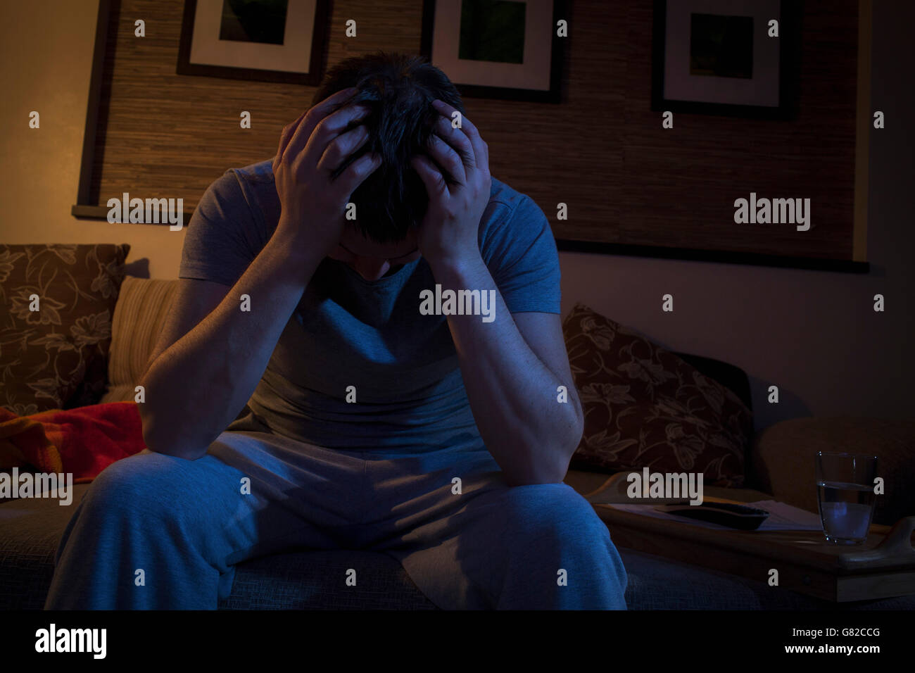 Front view of man with head in hands while sitting on sofa at home Stock Photo