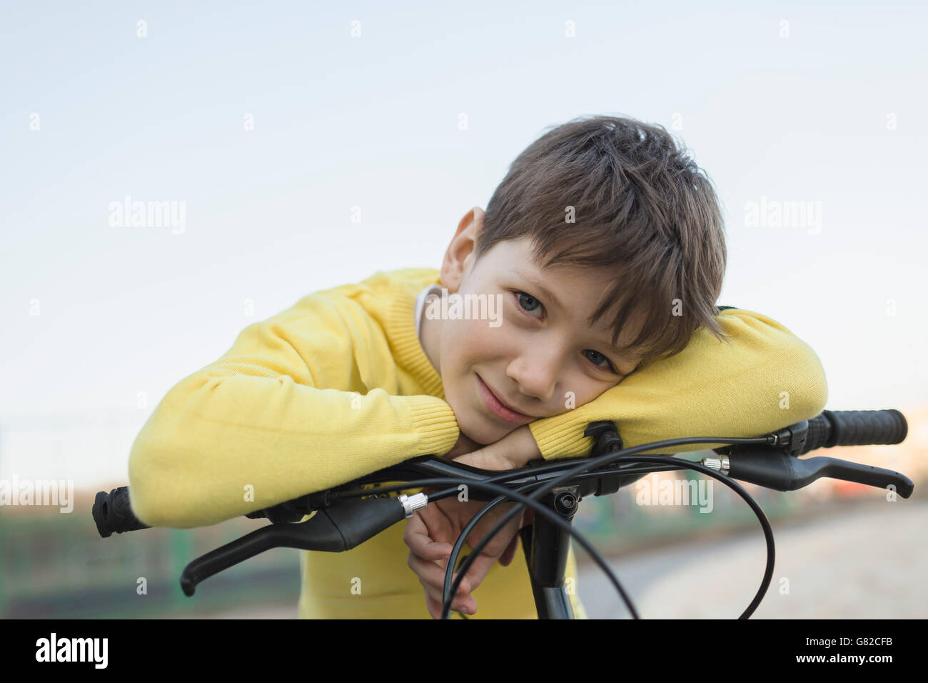 Portrait of smiling boy leaning on bicycle against clear sky Stock Photo