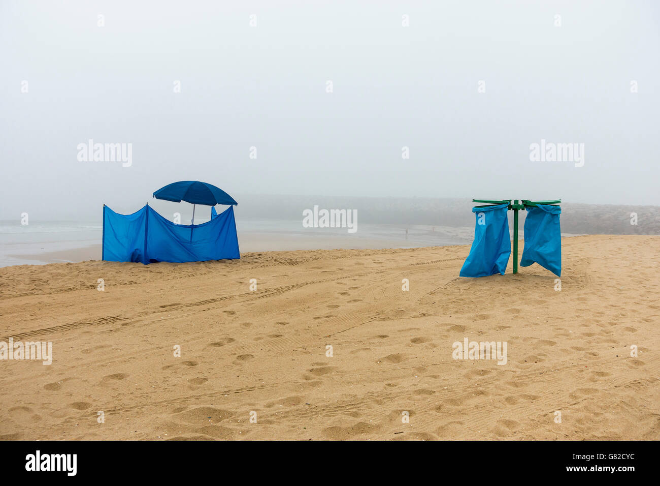 Blue tent and parasol by garbage bags at beach against sky during foggy weather Stock Photo