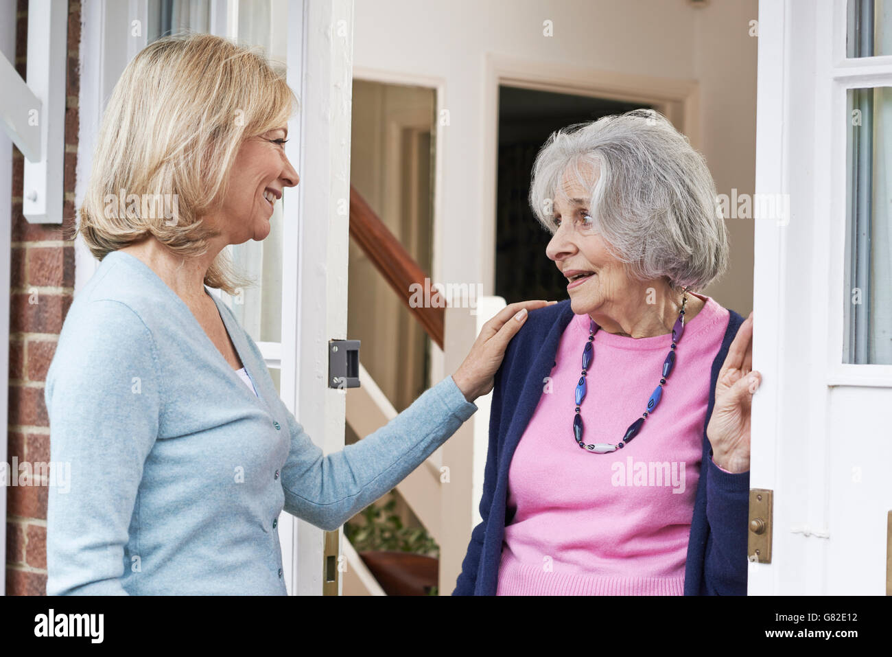 Woman Checking On Elderly Female Neighbor Stock Photo