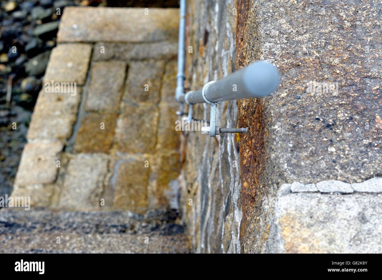 A handrail attached to a sea wall with steps down to the harbour Porthleven Cornwall England UK. Stock Photo