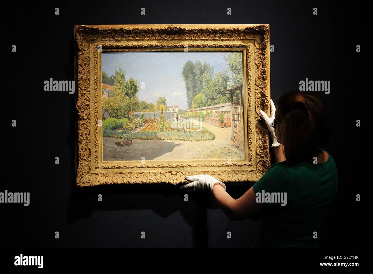 A Christie's employee looks at 'Le Potager', a painting by Alfred Sisley estimated between £1.5 million and £2 million, during a photo call for their Impressionist & Modern Art Evening Sale which is due to take place on 23rd June in London. Stock Photo