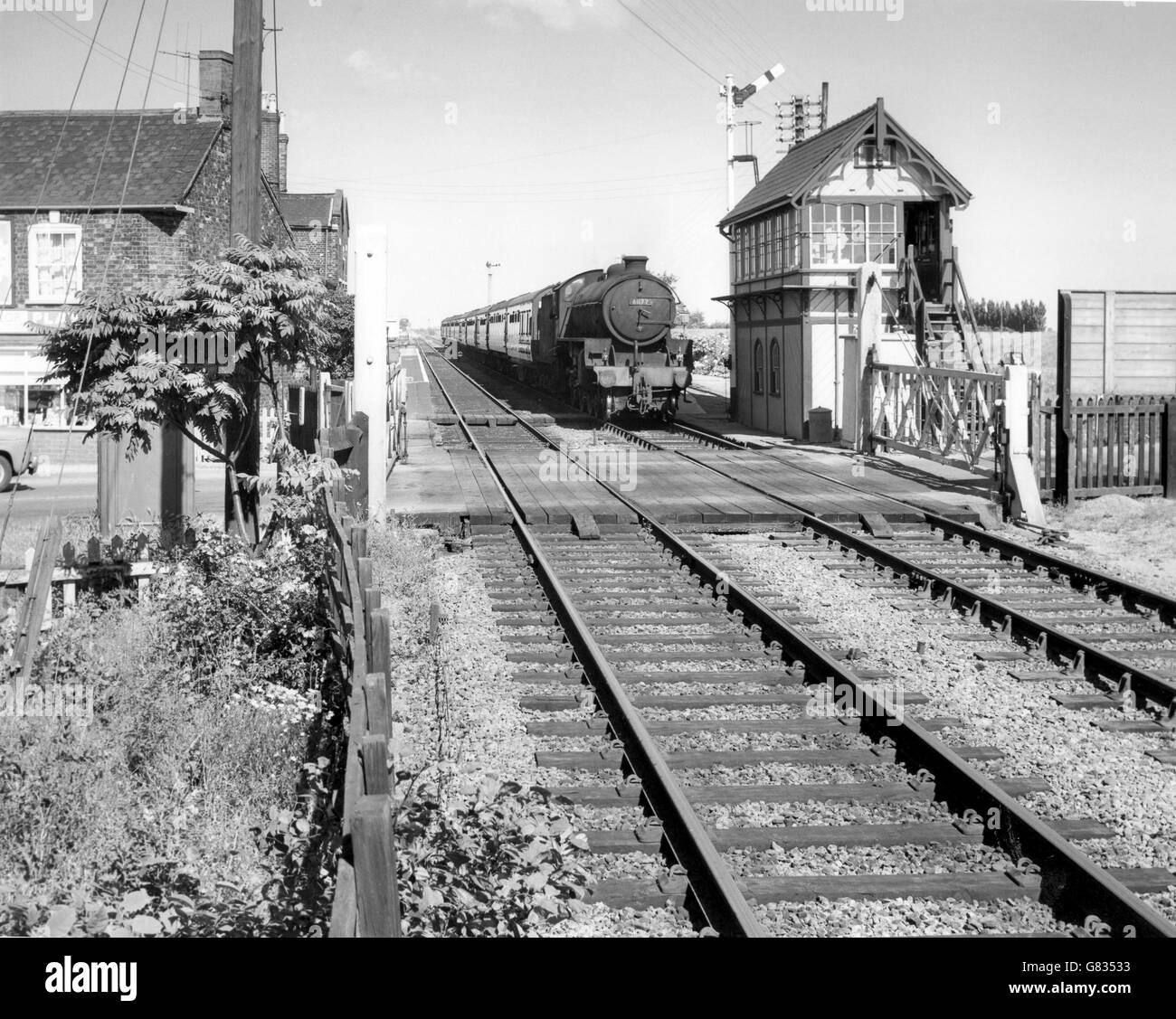 Thompson Class B1 at the head of a passenger train passes a signal box and level crossing at an unknown location in the east of Stock Photo