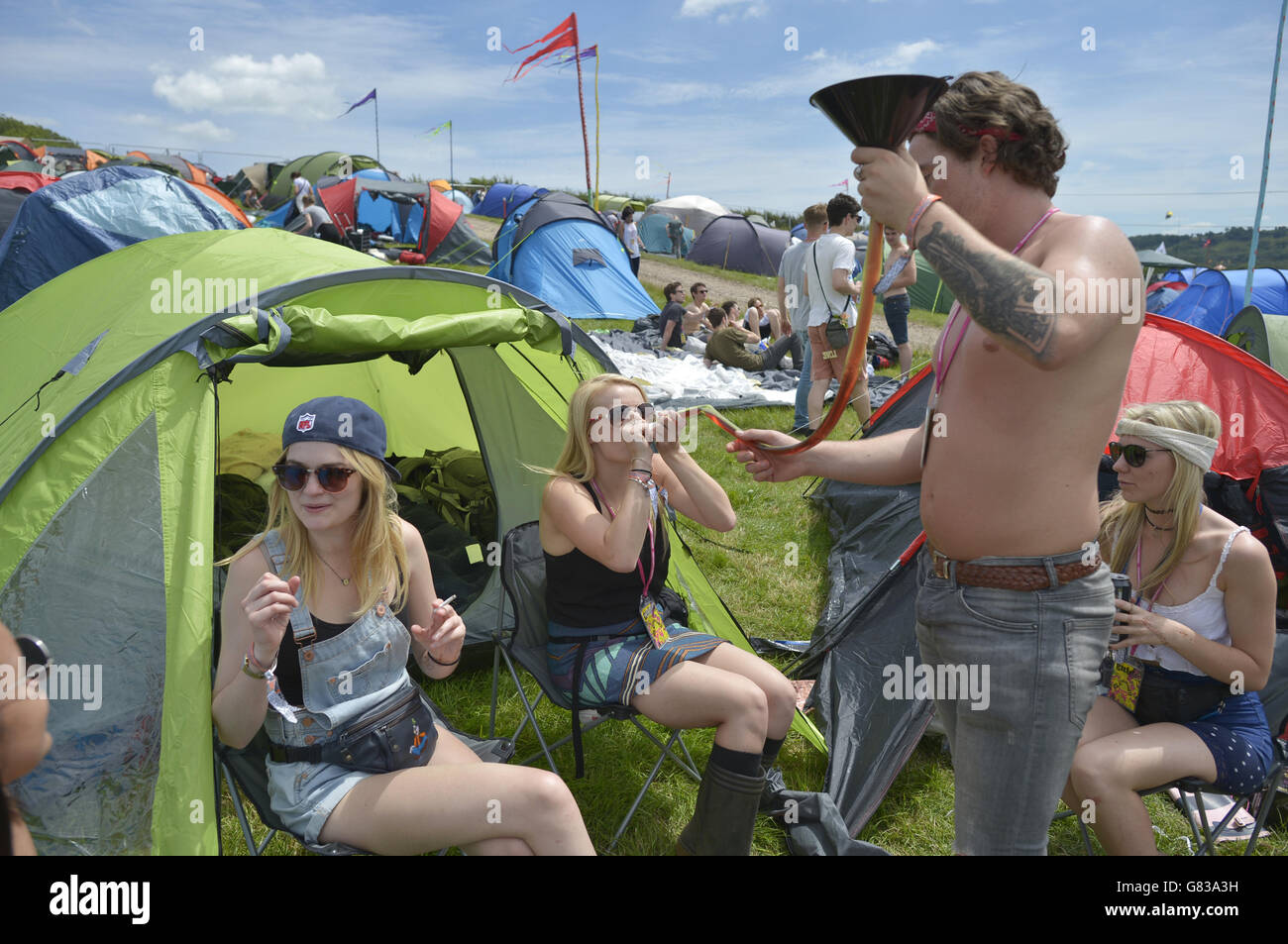 Chloe, 22, (surname not given) drunks fruit cider through a funnel and tube, also known as 'chugging' at the Glastonbury Festival, at Worthy Farm in Somerset. Stock Photo