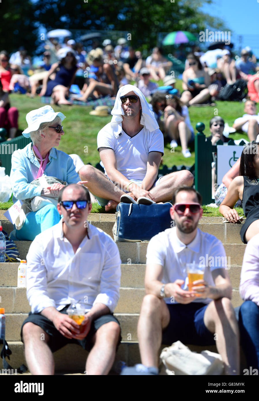 Spectators shield from the sun on Murray Mount during day two of the Wimbledon Championships at the All England Lawn Tennis and Croquet Club, Wimbledon. Stock Photo