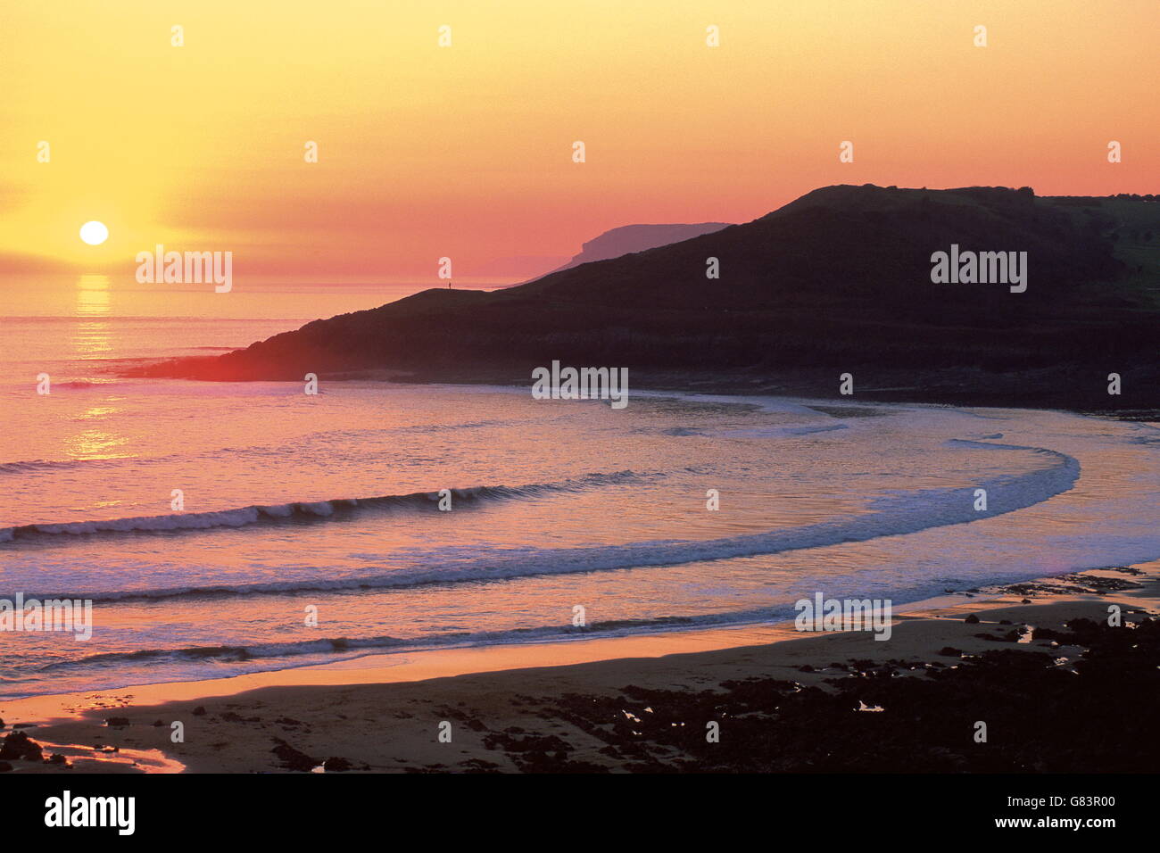 Classic orange sunset over beach .Waves curve into the bay below, sheltered by headlands. Stock Photo