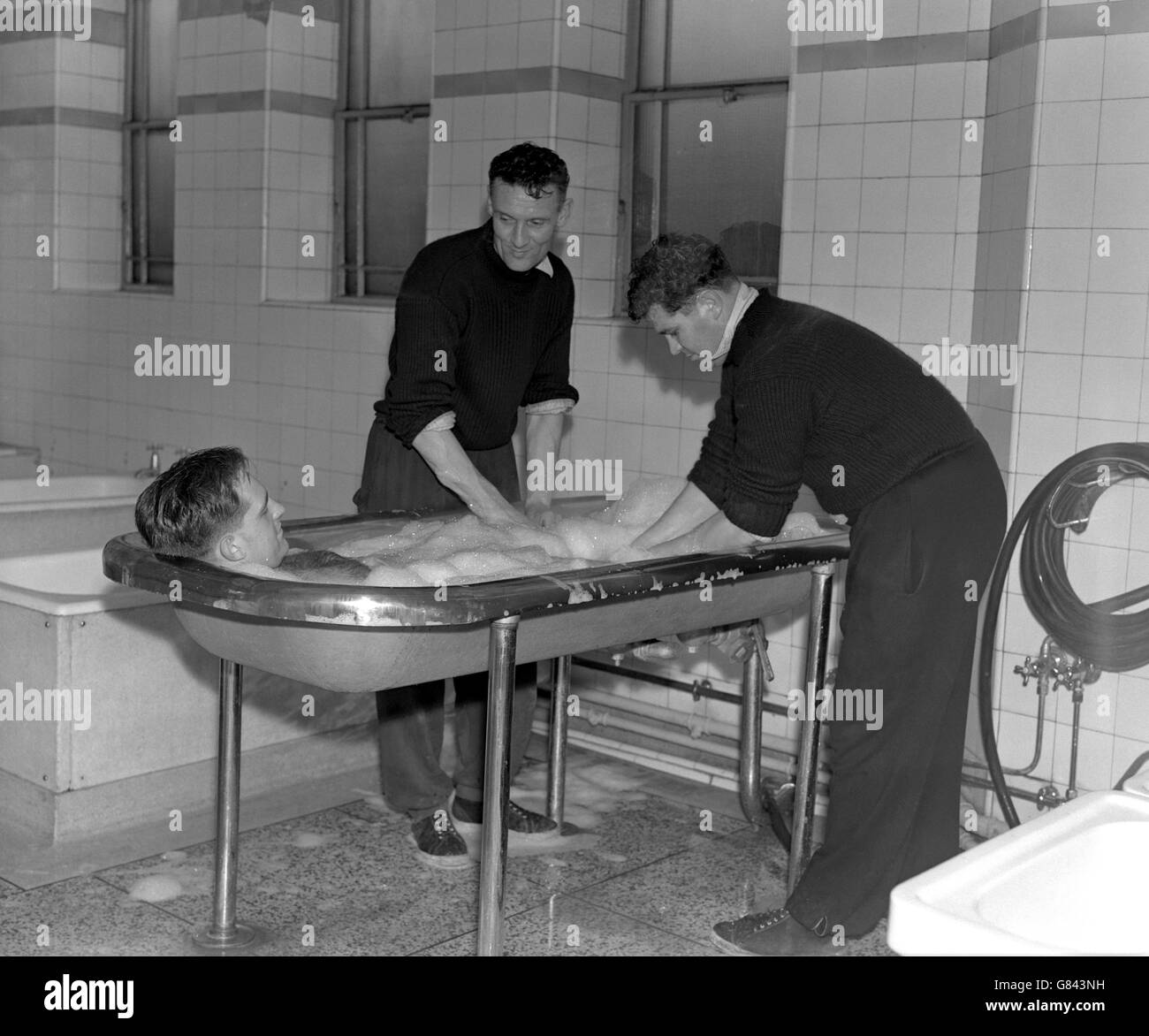 (L-R) Arsenal's Doug Lishman enjoys a soap foam bath massage, performed by coach Alf Fields and Les Compton. Stock Photo