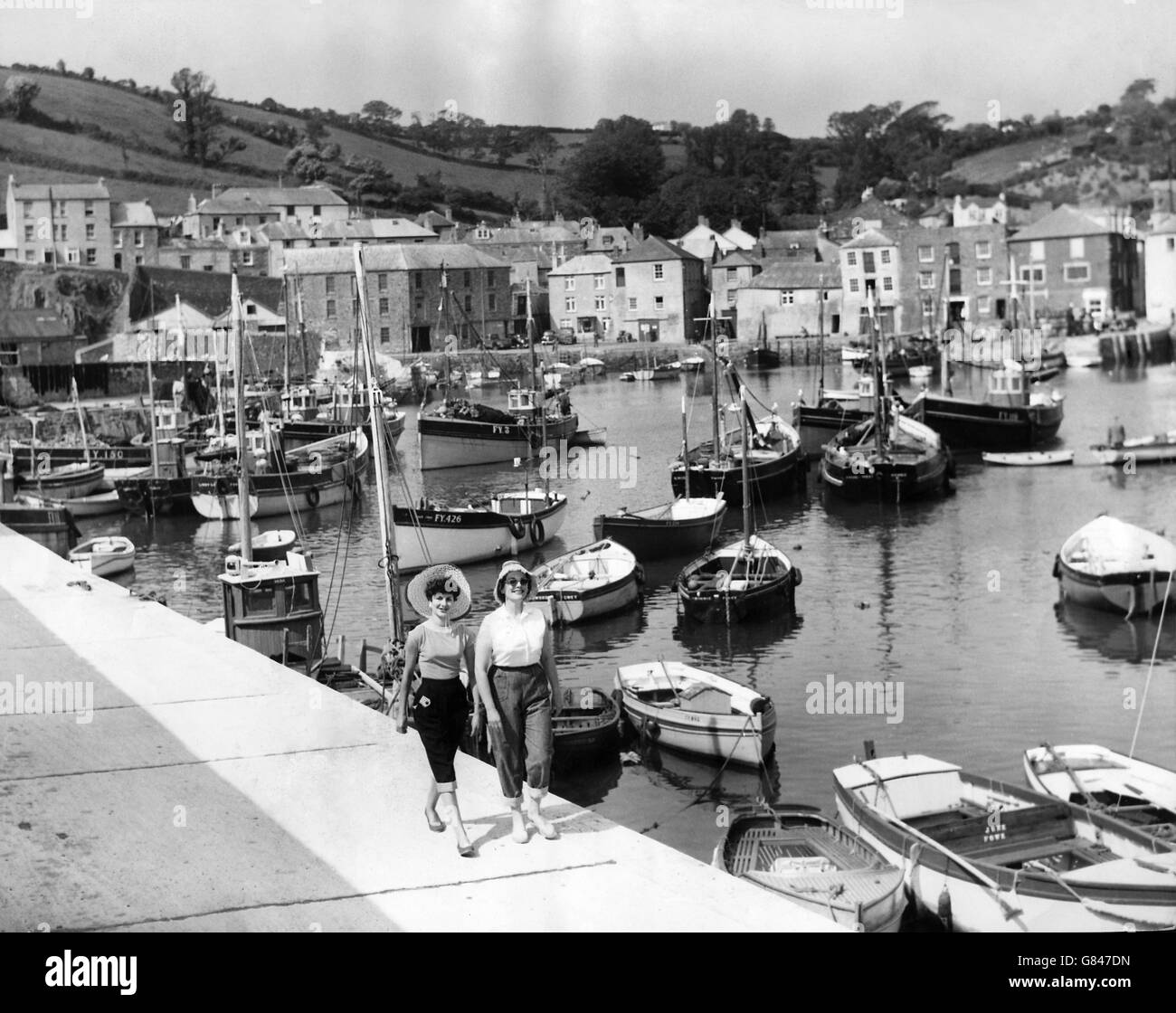 Two holidaymakers walk along the harbour wall at the old fishing port of Mevagissey in Cornwall. Stock Photo