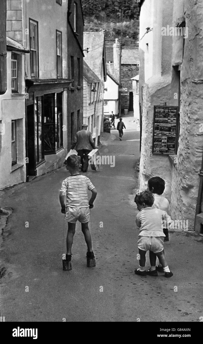 A young boy uses tin cans as stilts as children play down a small lane